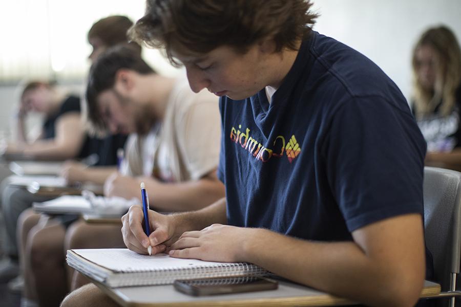 A student sits at a desk writing in a notebook.