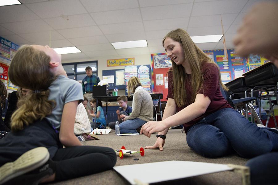 A young teacher sits on the ground with a child.