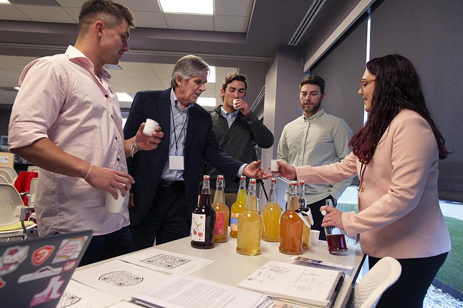 People gather around a table as a student hands out beverages.