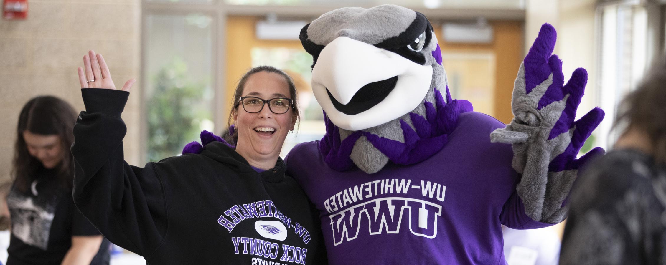 Willie Warhawk stands with a person in a 足彩平台 sweatshirt and they wave at the camera.